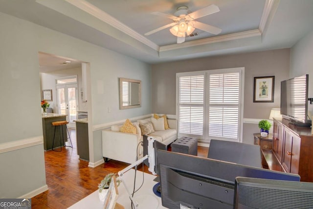 living area with visible vents, a raised ceiling, wood finished floors, and ornamental molding