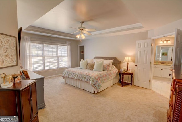 bedroom featuring a tray ceiling, light colored carpet, ensuite bathroom, a ceiling fan, and baseboards