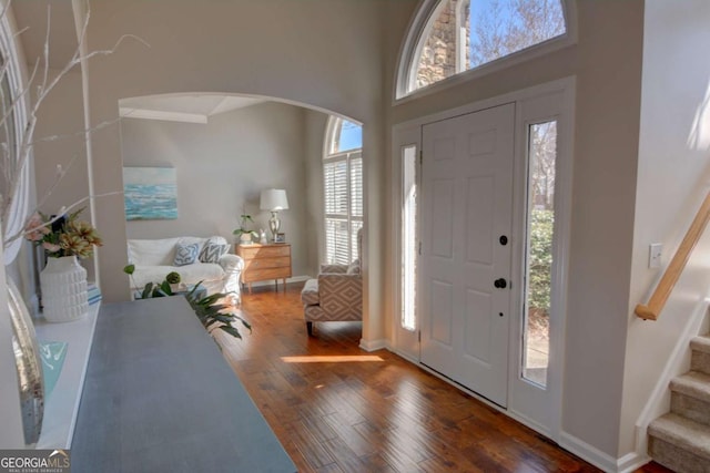 entrance foyer with arched walkways, stairway, a high ceiling, wood finished floors, and baseboards