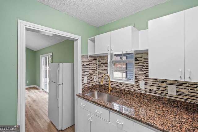 kitchen featuring backsplash, freestanding refrigerator, white cabinetry, a sink, and dark stone counters