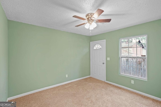 carpeted spare room featuring a textured ceiling, a ceiling fan, and baseboards