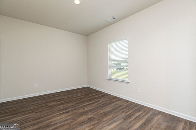 empty room featuring dark wood-style floors, visible vents, and baseboards