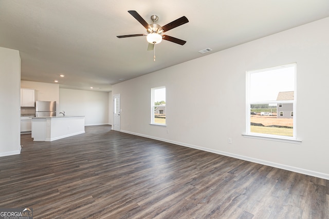 unfurnished living room with baseboards, visible vents, ceiling fan, and dark wood-style flooring