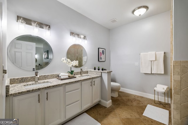 bathroom with toilet, double vanity, baseboards, and a sink