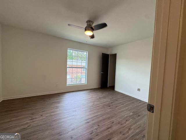 empty room with dark wood-style floors, a ceiling fan, and baseboards