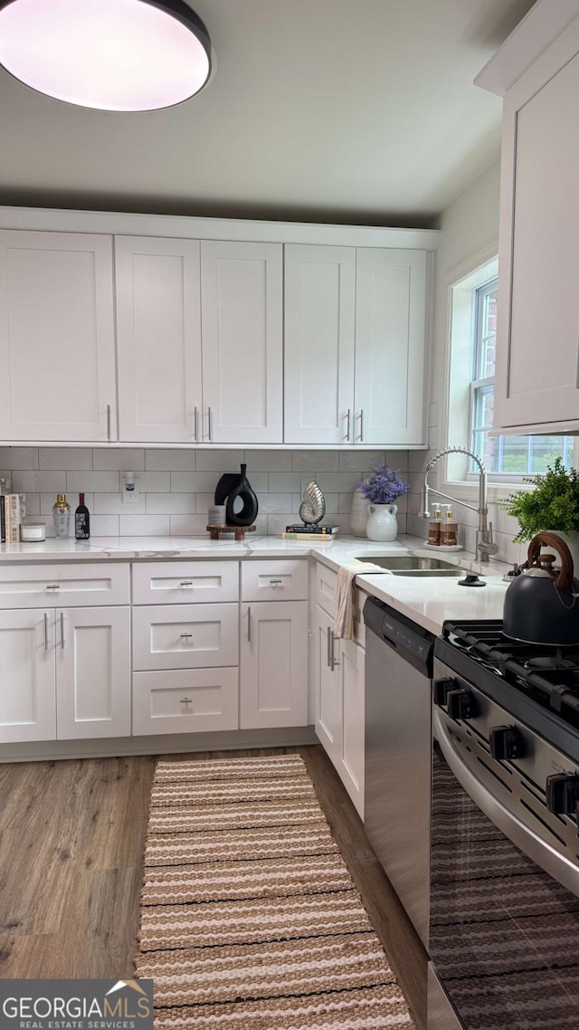 kitchen with wood finished floors, a sink, stainless steel appliances, white cabinetry, and backsplash