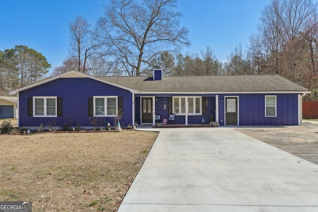 ranch-style house with a shingled roof, concrete driveway, board and batten siding, a chimney, and a front yard