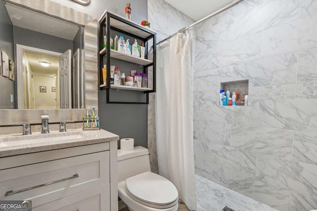 full bathroom with toilet, tiled shower, and vanity