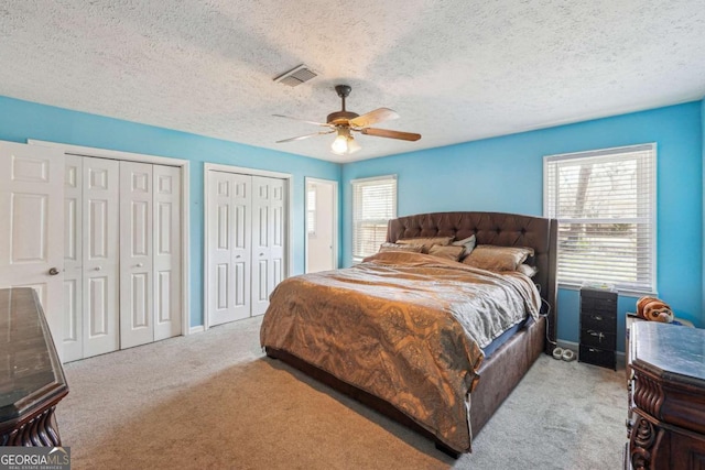 carpeted bedroom with ceiling fan, a textured ceiling, two closets, and visible vents