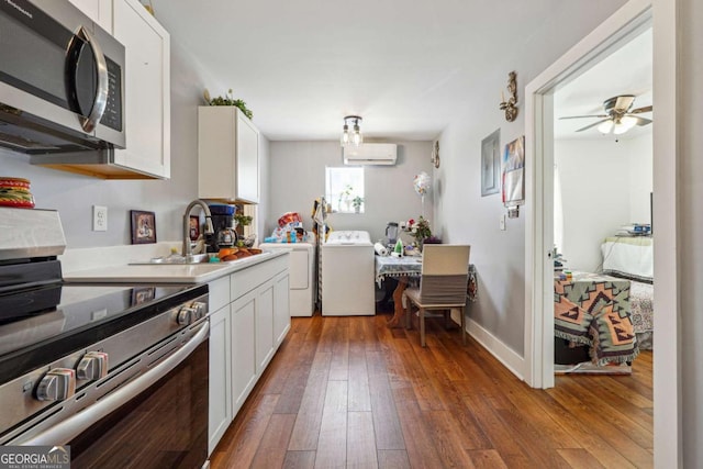 kitchen with washer / dryer, white cabinets, wood-type flooring, stainless steel appliances, and an AC wall unit