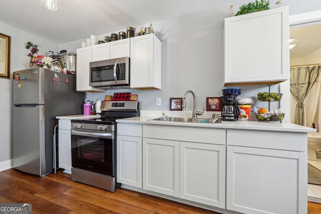 kitchen featuring appliances with stainless steel finishes, dark wood-style flooring, light countertops, white cabinetry, and a sink