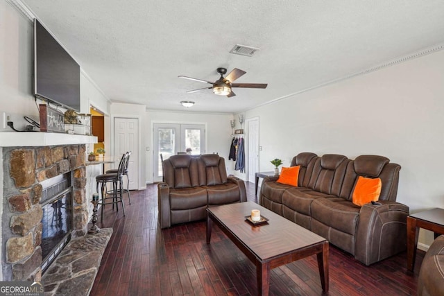 living area featuring dark wood-style flooring, a fireplace, visible vents, ceiling fan, and a textured ceiling