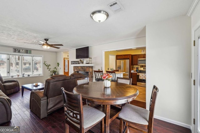 dining area featuring baseboards, visible vents, dark wood finished floors, a ceiling fan, and a fireplace