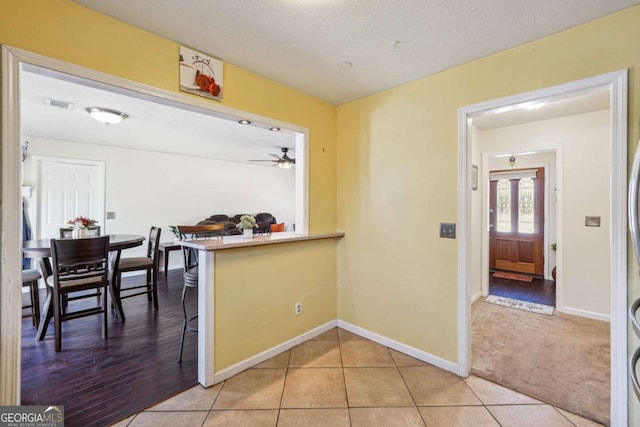 kitchen featuring light tile patterned floors, a textured ceiling, light colored carpet, visible vents, and baseboards