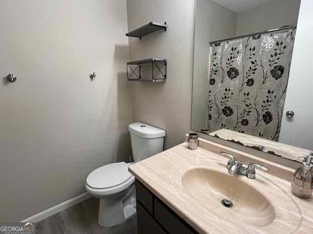 full bath with baseboards, a shower with shower curtain, toilet, wood finished floors, and vanity