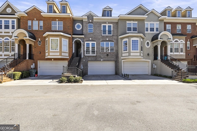 multi unit property featuring an attached garage, stairs, concrete driveway, and brick siding