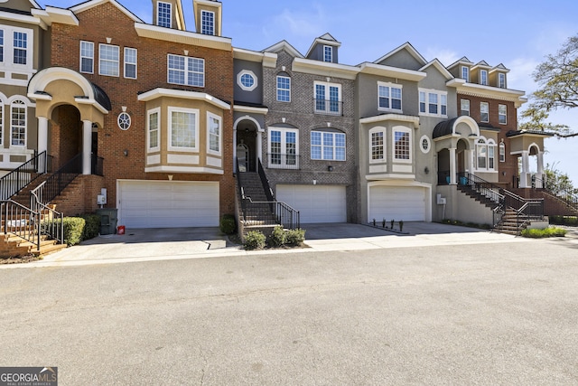 townhome / multi-family property featuring a garage, concrete driveway, brick siding, and stairway