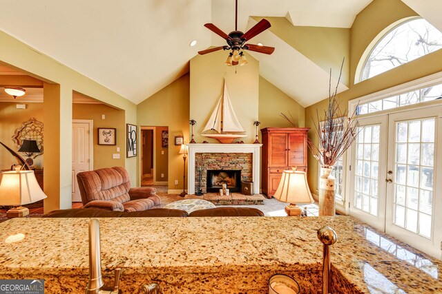living room featuring high vaulted ceiling, plenty of natural light, a ceiling fan, and a fireplace with raised hearth