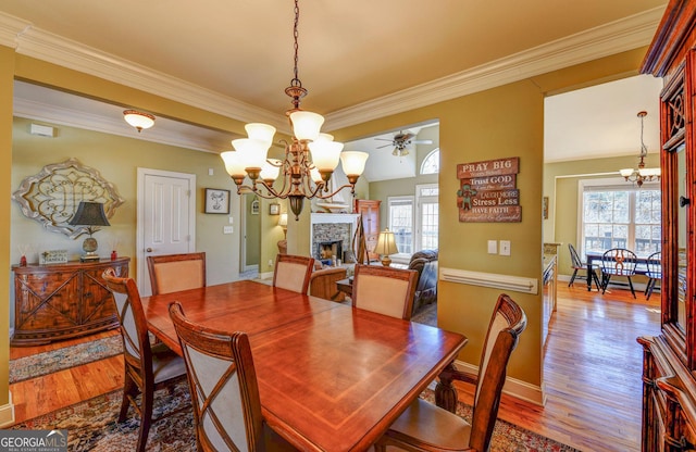 dining space featuring a chandelier, crown molding, wood finished floors, a fireplace, and a ceiling fan