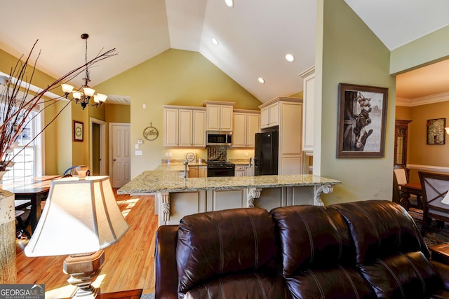 kitchen with black appliances, cream cabinets, light wood-style floors, light stone counters, and high vaulted ceiling