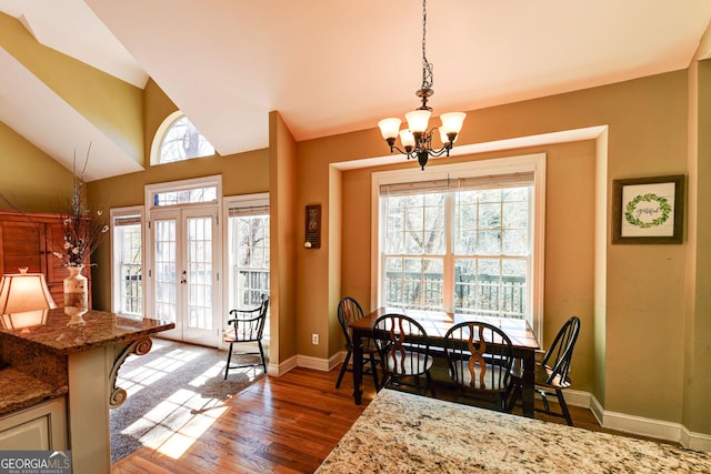 dining area featuring plenty of natural light, wood finished floors, baseboards, a chandelier, and vaulted ceiling
