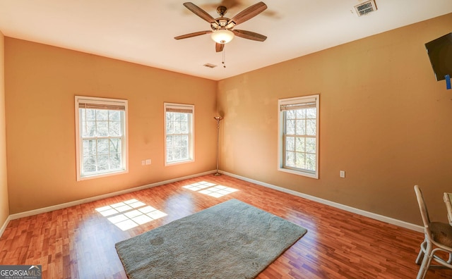 spare room with plenty of natural light, wood finished floors, visible vents, and baseboards