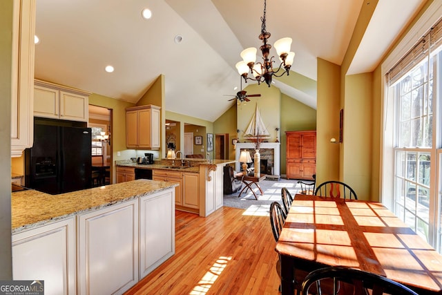 kitchen with a peninsula, cream cabinetry, black appliances, a fireplace, and a sink