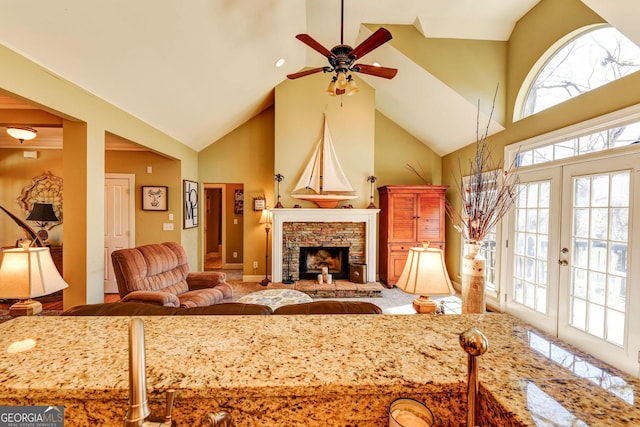 living area with a fireplace with raised hearth, high vaulted ceiling, french doors, and a ceiling fan