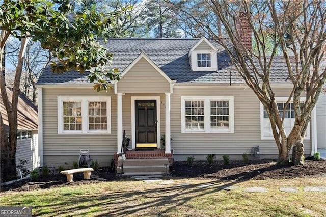 cape cod-style house with a chimney and roof with shingles