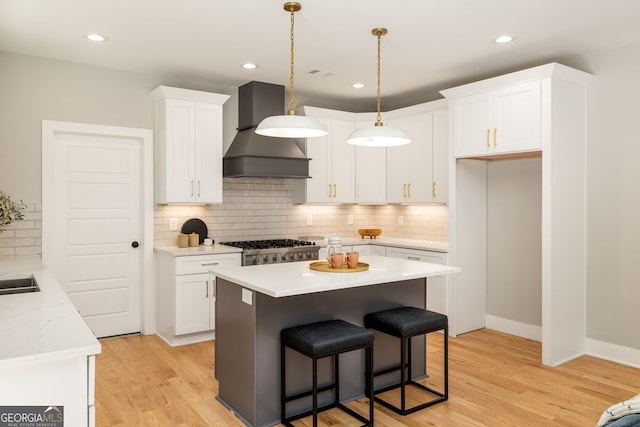 kitchen featuring wall chimney range hood, a center island, white cabinets, light wood finished floors, and hanging light fixtures