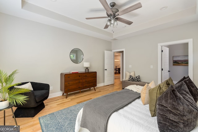 bedroom with ceiling fan, a raised ceiling, baseboards, and wood finished floors