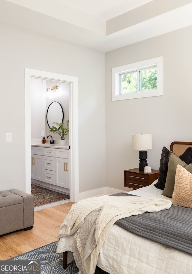 bedroom with ensuite bath, light wood-style floors, and a sink