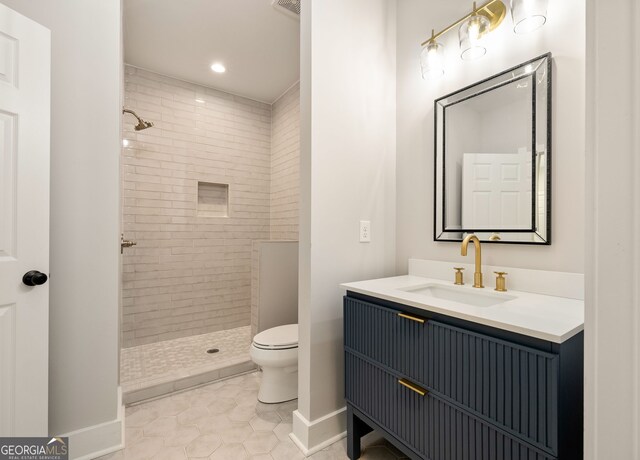 bathroom with baseboards, toilet, tiled shower, tile patterned floors, and vanity