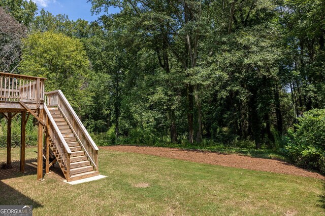 view of yard with a wooded view, a wooden deck, and stairs