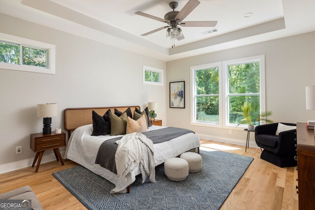 bedroom featuring a raised ceiling, baseboards, visible vents, and light wood finished floors