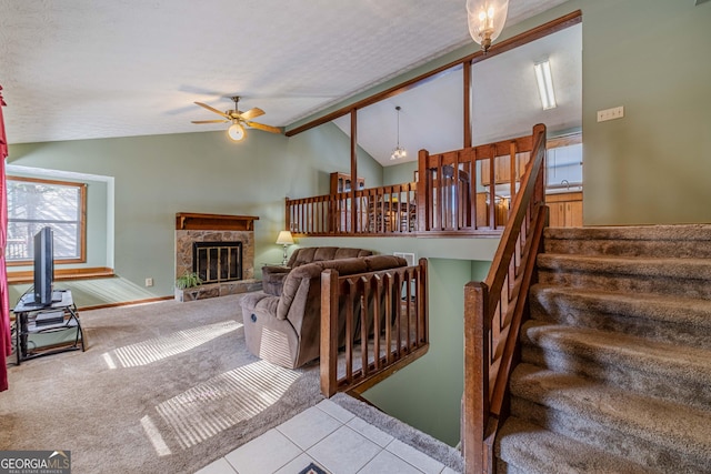 living area with lofted ceiling with beams, carpet floors, a ceiling fan, stairs, and a glass covered fireplace