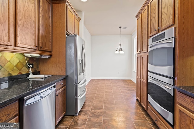 kitchen featuring brown cabinets, stainless steel appliances, backsplash, dark stone counters, and baseboards