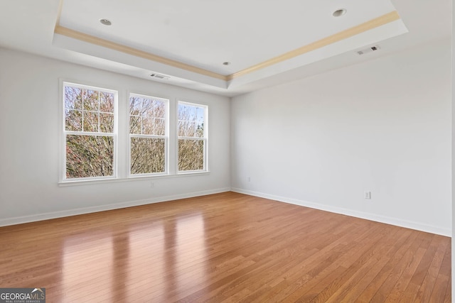 spare room with light wood-type flooring, a raised ceiling, and visible vents