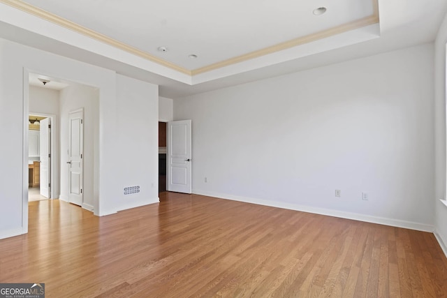 interior space featuring light wood-type flooring, a tray ceiling, ornamental molding, and baseboards