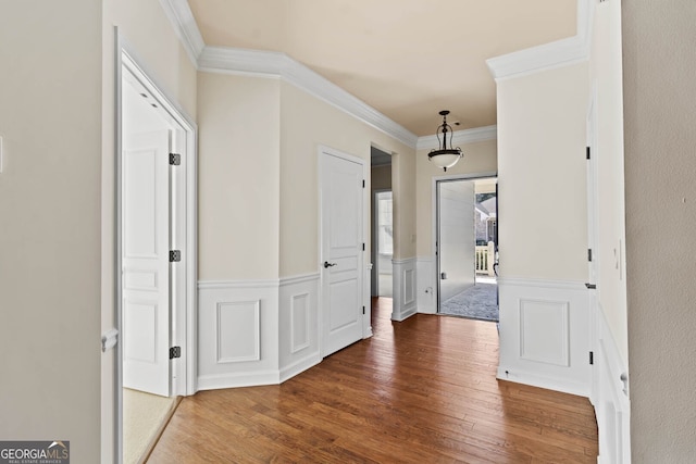 corridor featuring wood-type flooring, ornamental molding, and wainscoting