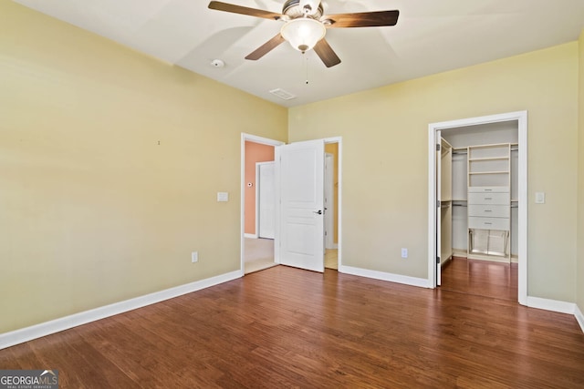 unfurnished bedroom featuring a spacious closet, wood finished floors, and baseboards