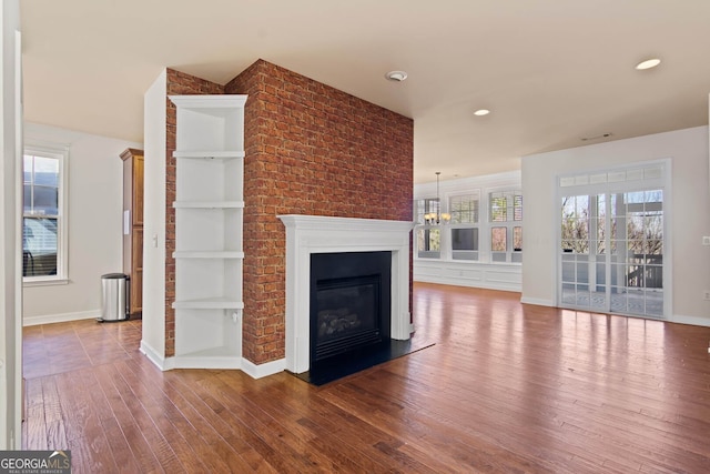 unfurnished living room featuring a wealth of natural light, baseboards, a glass covered fireplace, and hardwood / wood-style floors