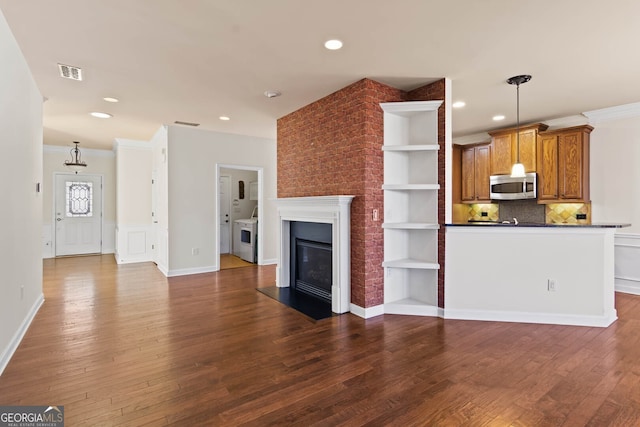 unfurnished living room with dark wood-type flooring, a glass covered fireplace, visible vents, and ornamental molding