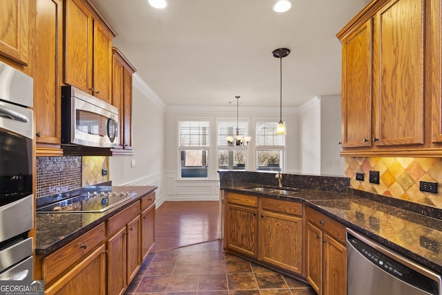 kitchen with brown cabinetry, wainscoting, ornamental molding, stainless steel appliances, and a sink