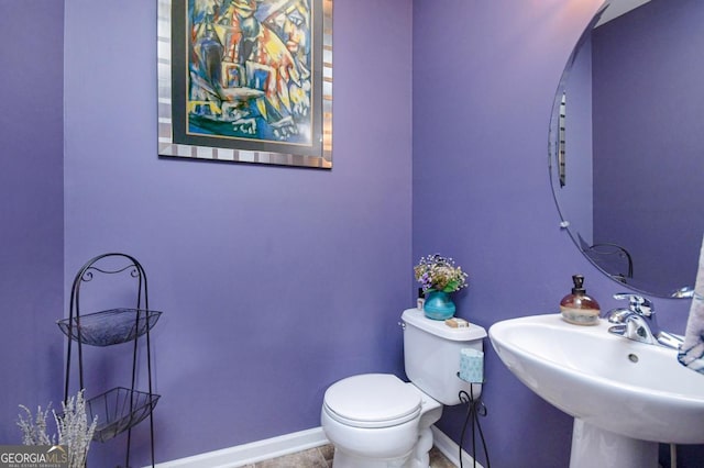 half bath featuring baseboards, a sink, and toilet