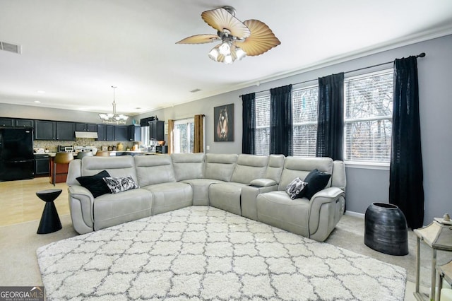 living room featuring ceiling fan with notable chandelier, baseboards, visible vents, and light colored carpet