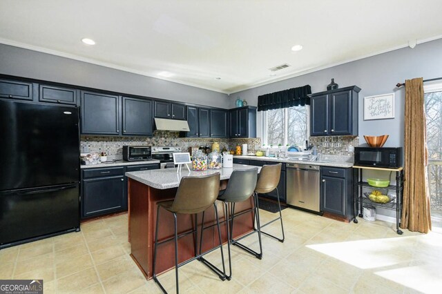 kitchen featuring a breakfast bar area, light countertops, decorative backsplash, under cabinet range hood, and black appliances