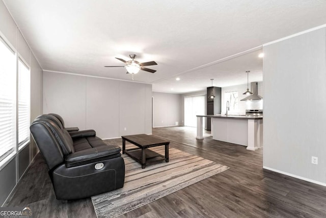 living area with dark wood-style floors, ornamental molding, a ceiling fan, and baseboards