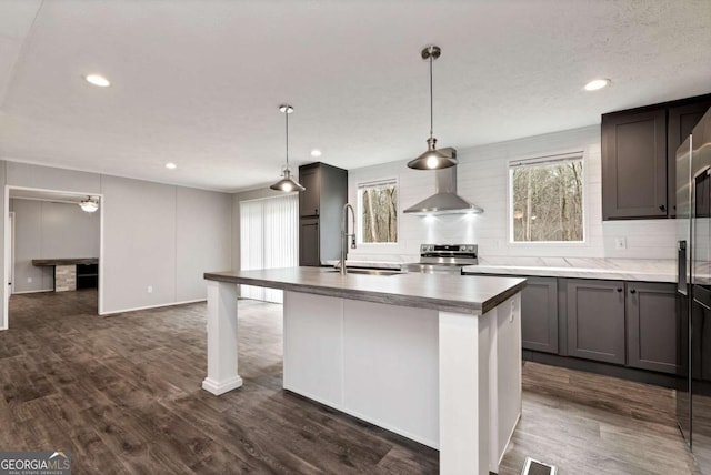 kitchen featuring a sink, stainless steel range with electric cooktop, backsplash, wall chimney exhaust hood, and dark wood finished floors