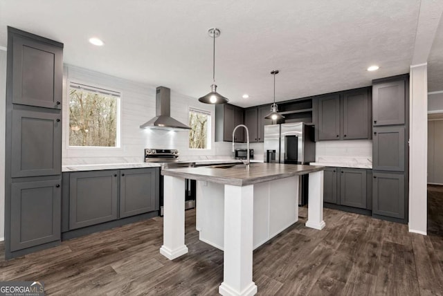 kitchen with wall chimney exhaust hood, appliances with stainless steel finishes, dark wood-style flooring, and gray cabinetry